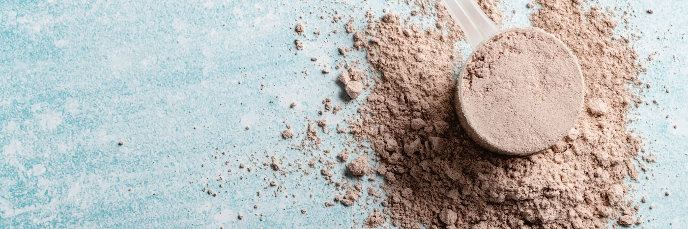 A measuring scoop of drink powder tipped out across a pale blue surface.