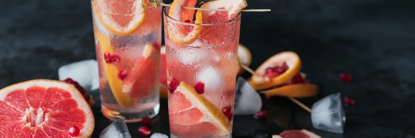 Two tall glasses of a grapefruit and pomegranate mocktail over ice on a slate board.