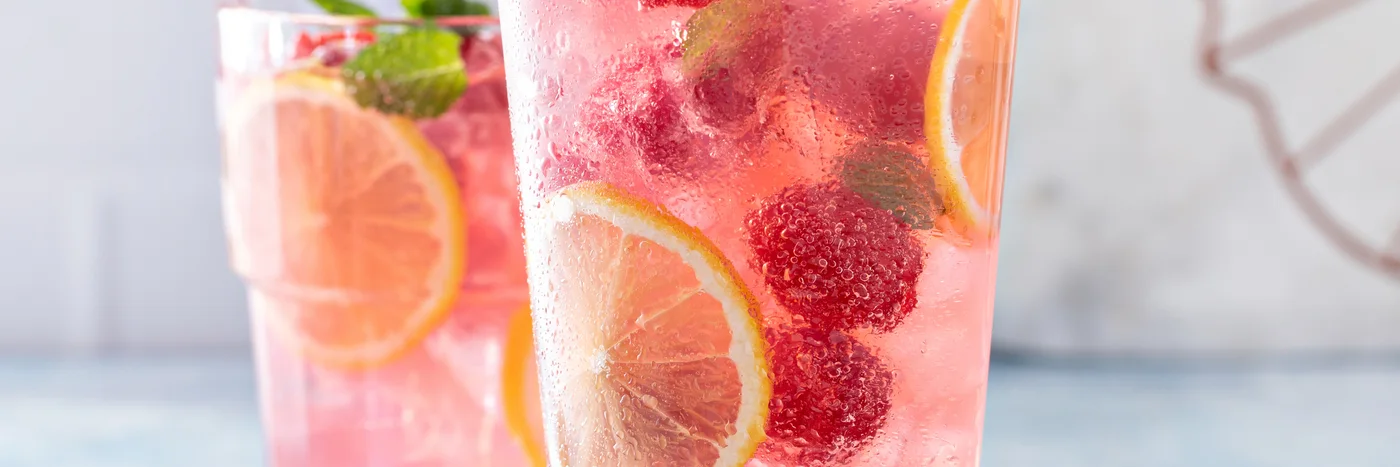 Two tall glasses of a pink non-alcoholic spritz with citrus slices and raspberries over ice.