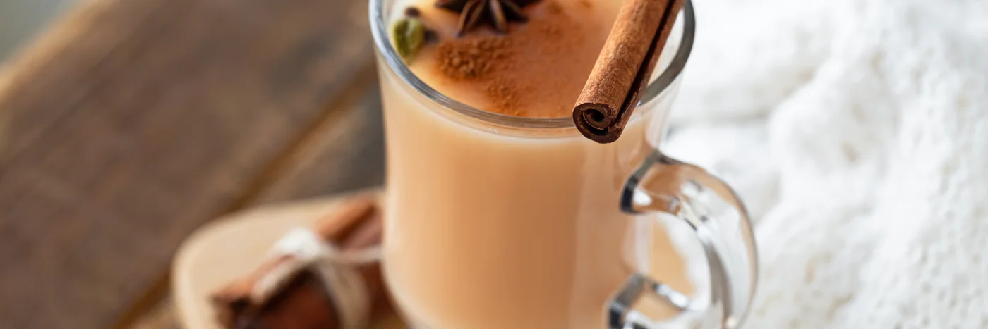 A glass mug of spiced masala chai topped with cinnamon and star anise on a wooden board.